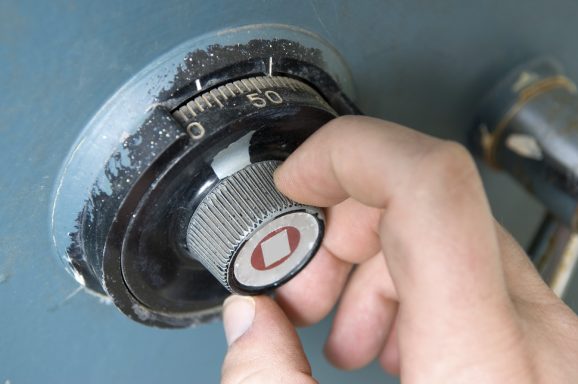 Une main tourne un bouton de combinaison d'un coffre-fort usé.