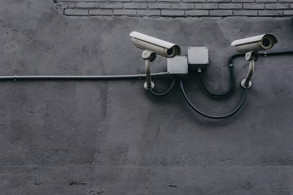 Deux caméras de surveillance fixées sur un mur gris avec des câbles.